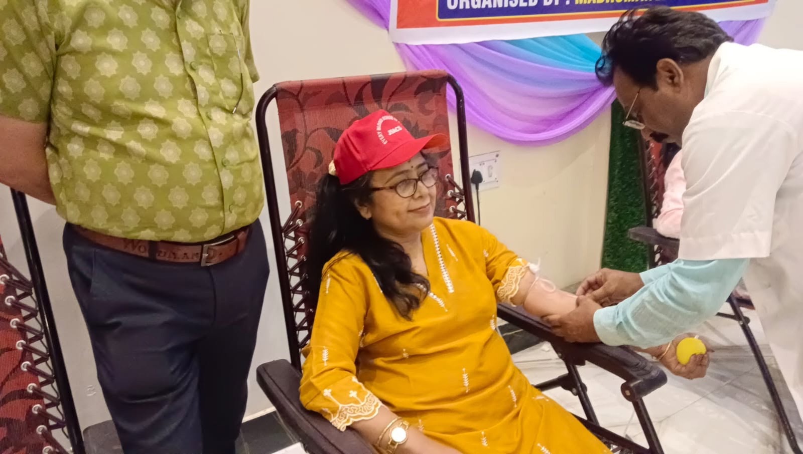 A woman in a red cap donating blood, assisted by a technician